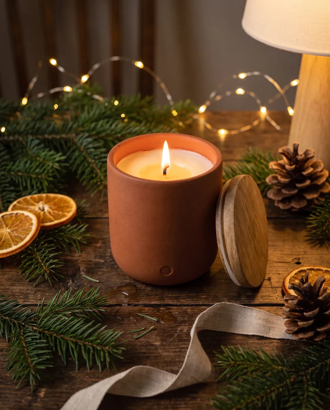 La même bougie allumée, entourée de branches de sapin, de tranches d'orange séchées et de guirlandes lumineuses