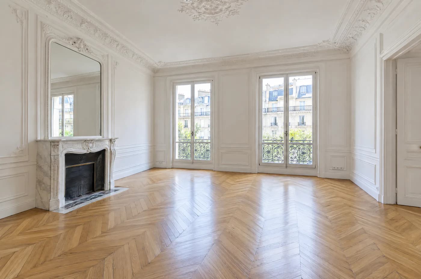 Salon haussmannien vide : moulures, parquet en point de Hongrie, cheminée en marbre et portes-fenêtres